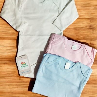 Três bodies de bebé em branco, rosa e azul claro com etiquetas com o texto Pirulinhos, sobre madeira clara.