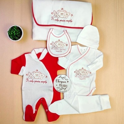 Conjunto de roupa de bebé com bordados de coelhinhos e texto em vermelho, disposto sobre mesa clara com pequeno vaso verde.