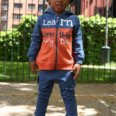 Criança com fato de treino azul e laranja, ténis brancos e skate preto ao ar livre