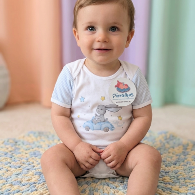 Bebé sentado em tapete malhado usando body branco e azul com estampa de coelho e carro