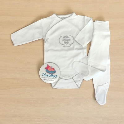 Conjunto de bebé branco com body e calças sobre superfície de madeira clara