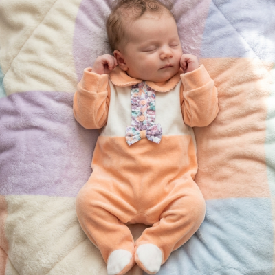 Bebé a dormir com fato pêssego e branco com laço, sobre manta pastel