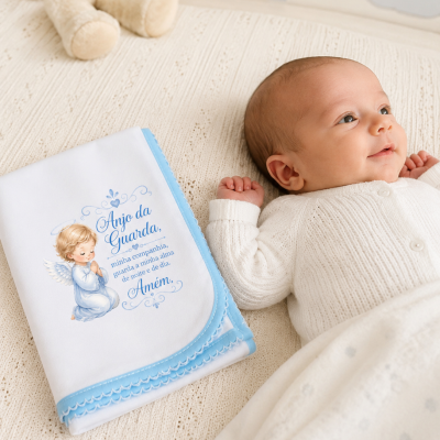 Manta branca e azul com ilustração de anjo e texto, bebé deitado em cama bege com padrão de nuvens
