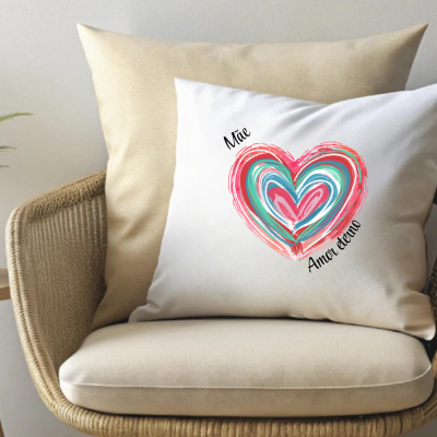 Almofada branca com estampa de coração colorido e texto, numa cadeira de rattan com almofada bege.