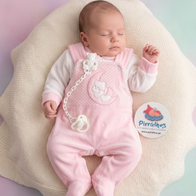Bebé com macacão rosa e chupeta branca deitado sobre manta creme ao lado de cartão redondo pirralhos