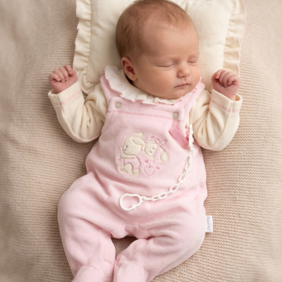 Bebé dormindo com fato cor-de-rosa e bordado de coelhos, deitado sobre almofada e manta bege.