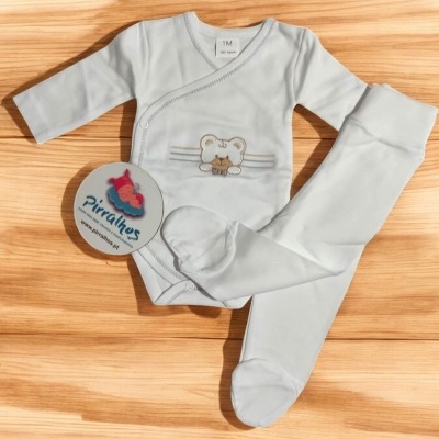 Conjunto branco de bebé com body e calças, sobre madeira clara