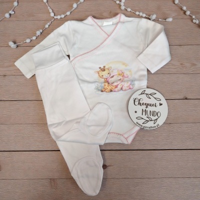Conjunto de roupa de bebé branco com estampa de girafa e bebé, etiqueta com texto, decorado com guirlanda branca e fundo de madeira.