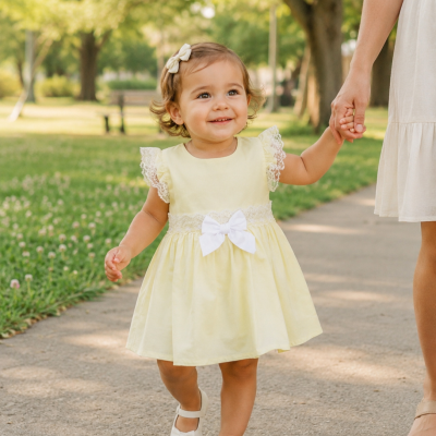 Criança com vestido amarelo claro e sapatos brancos a andar ao ar livre.