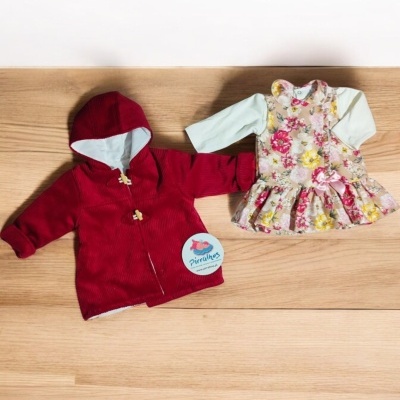 Conjunto infantil com casaco vermelho e vestido floral sobre madeira clara