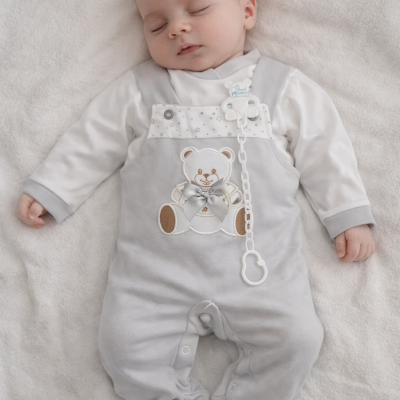 Bebé com macacão cinzento com estampa de urso deitado numa manta branca