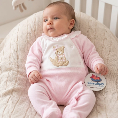 Bebé com macacão rosa e branco com ursinhos bordados, deitado em almofadão creme de malha, segurando etiqueta Pirralhos