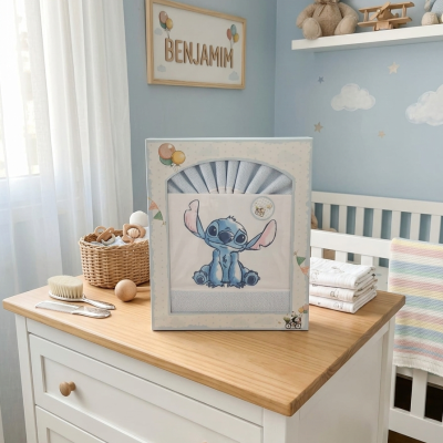 Conjunto de tecido com estampa Stitch em quarto de bebé com parede azul, quadro BENJAMIM, móvel branco e objetos de bebé.