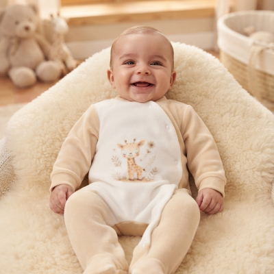 Bebé sorridente de pijama bege e branco com desenho de girafa sentado em almofada macia