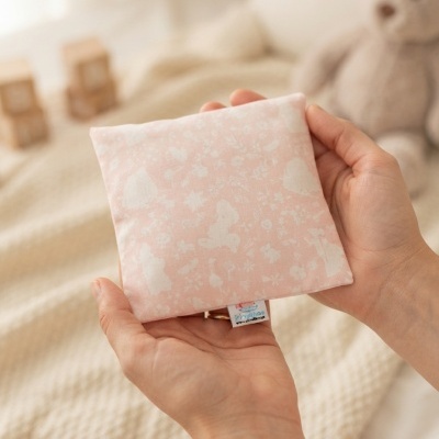Almofada pequena rosa com padrão branco e fundo com manta, cubos de madeira e ursinho peluche