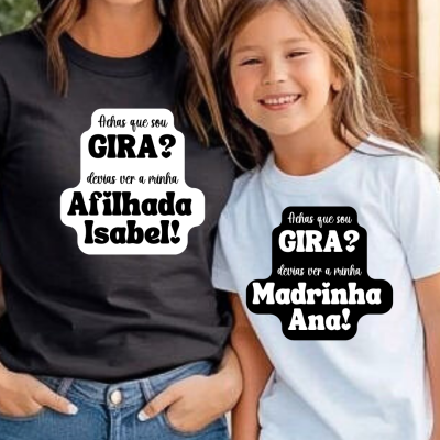 Camisolas preta e branca com textos personalizados sobre afilhada e madrinha, usadas por uma mulher e uma menina sorridentes.