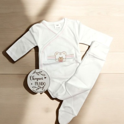 Pijama branco de bebé com ursinho bordado e riscas cor-de-rosa sobre chão de madeira clara