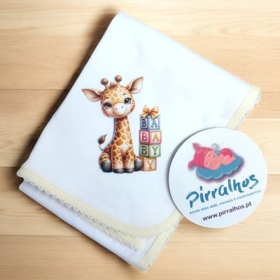 Fralda branca com girafa e blocos de letras, borda em croché creme, sobre madeira clara com adesivo da marca Pirralhos