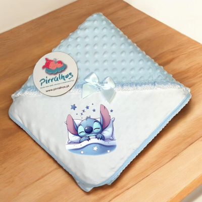 Manta de bebé azul com personagem Stitch a dormir, laço branco e renda, sobre madeira