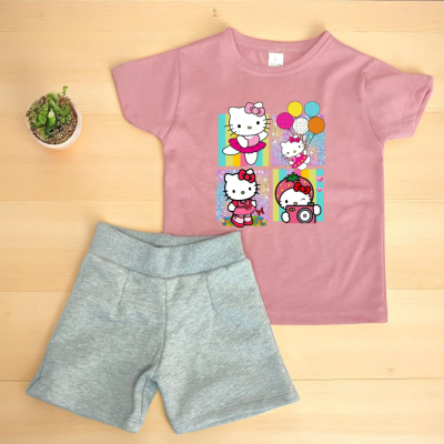 Conjunto infantil rosa Hello Kitty e calções cinza sobre madeira clara com planta ao lado.
