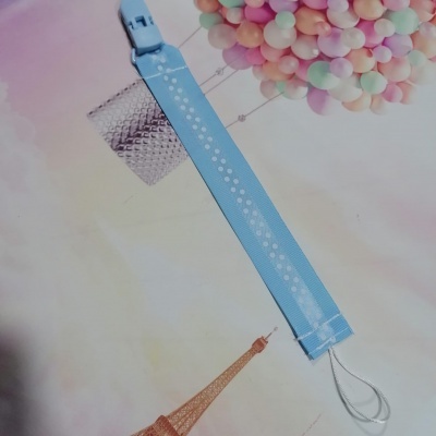 Pulseira azul claro de tecido com padrão de bolinhas e fecho de plástico em fundo com Torre Eiffel e balão colorido