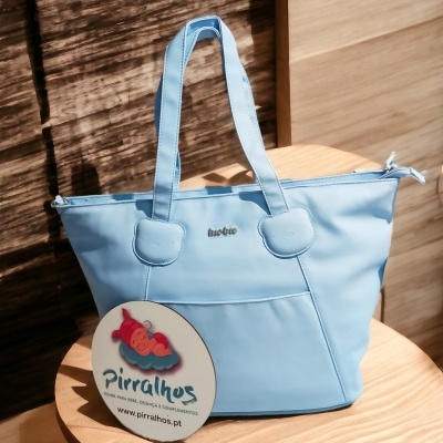 Mala de mão azul claro com alças e bolso frontal sobre cadeira de madeira clara