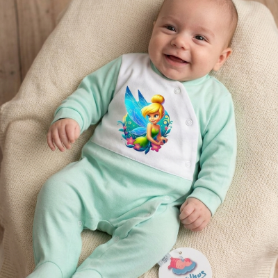 Bebé com pijama verde água e branco com imagem de fada sentado em tecido bege.
