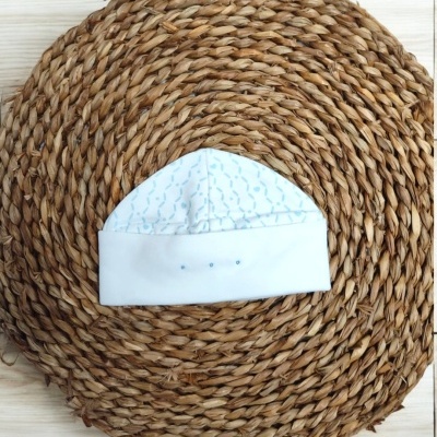 Touca branca para bebé com padrão azul claro sobre tapete redondo de fibras naturais