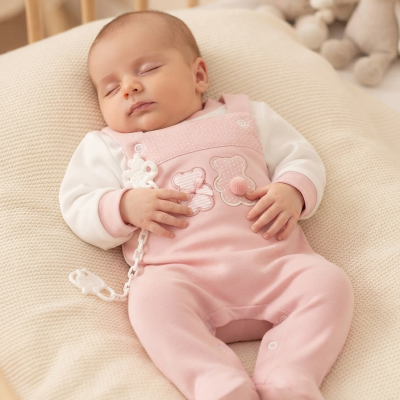 Bebé a dormir com babygrow cor-de-rosa e branco sobre almofada bege