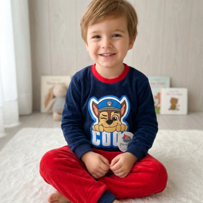 Criança sentada no chão a usar pijama azul escuro e vermelho com imagem de cão policial e a palavra COOL