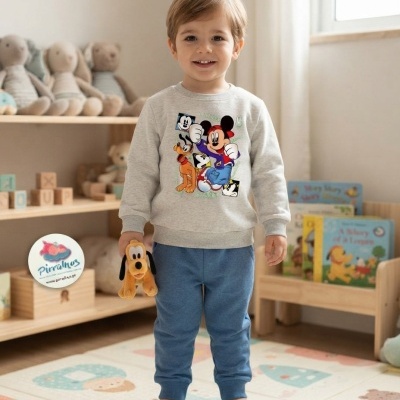 Criança com camisola cinza com estampa Mickey e calças azuis num quarto infantil