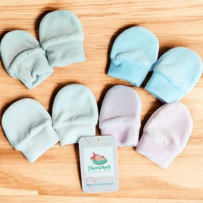 Luvas para bebé em várias cores claras com etiqueta Pirilahes em fundo madeira