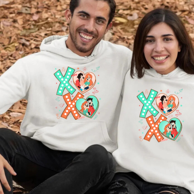 Dois jovens sentados ao ar livre com sweatshirts brancas com design colorido XOXO e ilustrações de casais