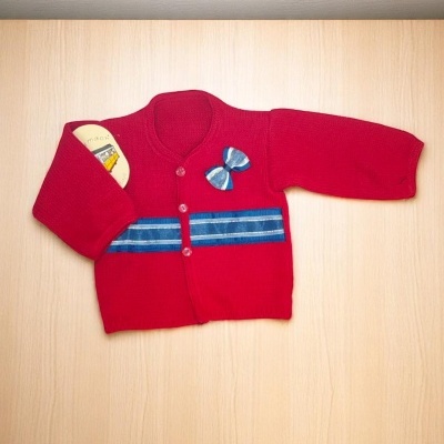 Casaco infantil vermelho com detalhes em azul sobre superfície de madeira clara