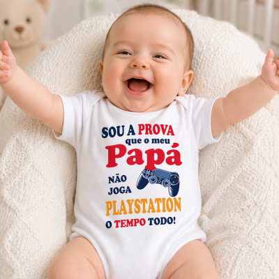 Body branco para bebé com texto colorido e comando de videojogo, bebé sorridente sentado num sofá claro.