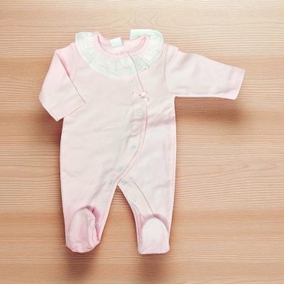 Macacão rosa bebé com gola branca e botões numa mesa de madeira clara.