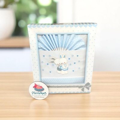 Caixa com toalha azul com coelho bordado e selo Pirralhos em mesa de madeira