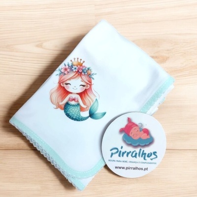 Manta branca com sereia estampada e cartão da marca Pirralhos num fundo de madeira clara