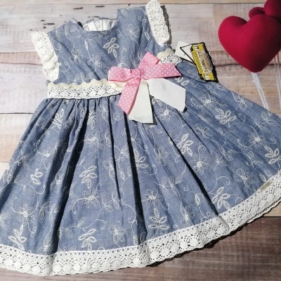 Vestido infantil azul com padrão floral branco e renda branca, laço rosa e branco, etiqueta e balões de coração vermelhos