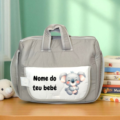 Bolsa cinzenta para bebé com bolso branco e ilustração de coala, junto a livros infantis e peluche.