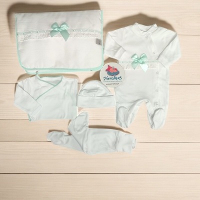 Conjunto de roupa de bebé branco com detalhes em verde água e renda, sobre superfície de madeira clara