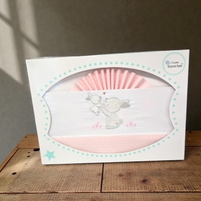 Conjunto de roupa de bebê rosada e branca com bordado de coelhos em caixa branca com estrelas azuis