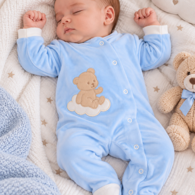 bebé a dormir com pijama azul e ursinho bordado numa cama com colcha de estrelas e manta azul