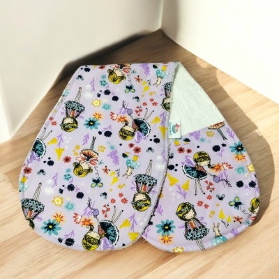 Dois panos de cozinha com padrão de bonecas e flores sobre mesa de madeira clara