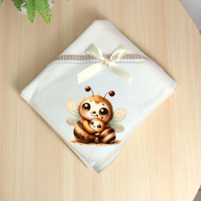 Manta branca com bordado de duas abelhas carinhosas e laço creme sobre mesa de madeira