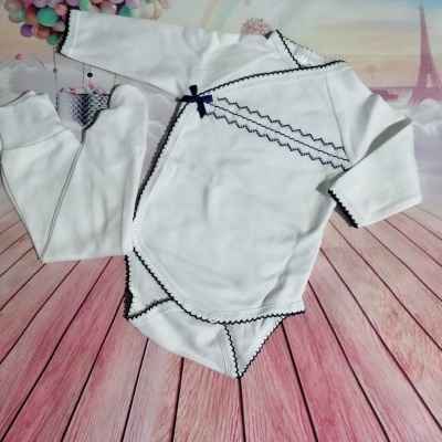 Roupa de bebé branca com detalhes pretos num fundo com Torre Eiffel e balões