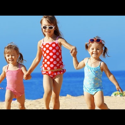 Três crianças com fatos de banho e óculos de sol na praia