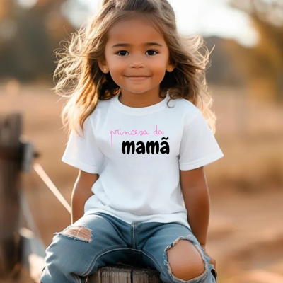 Menina sentada numa cerca de madeira a usar camisola branca com texto e calças azuis rasgadas