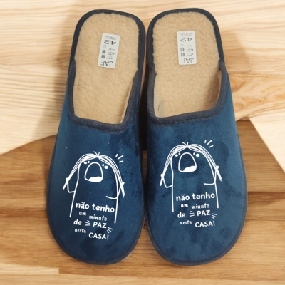 Chinelos azuis com interior felpudo bege e frase estampada em branco sobre chão de madeira claro
