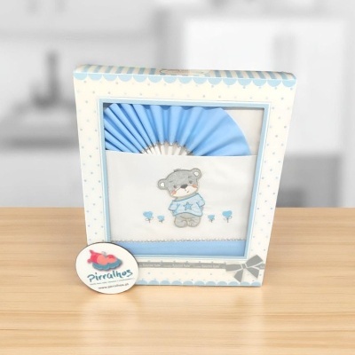 Fralda branca com desenho de urso e flores azuis em embalagem azul claro com bolinhas.